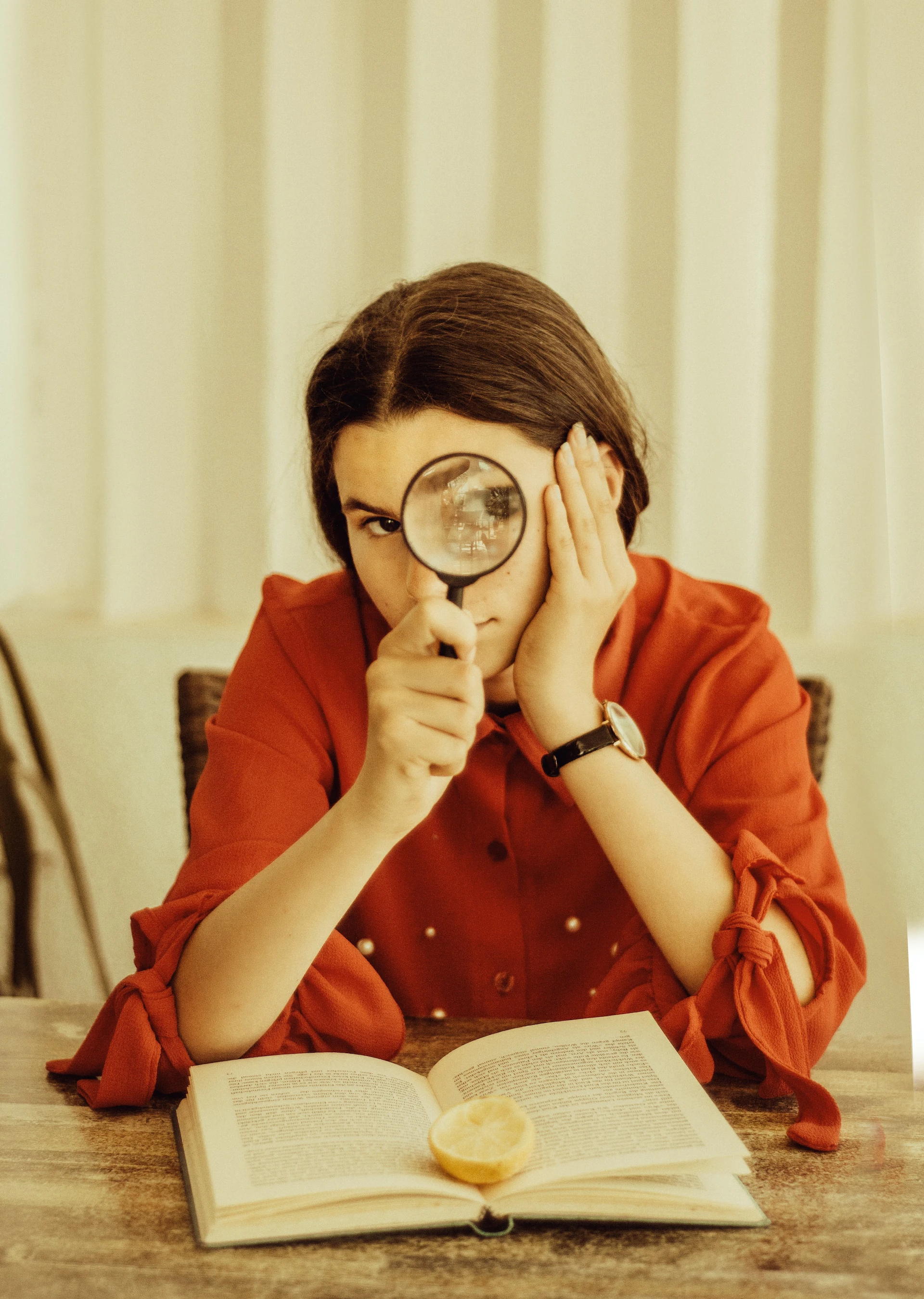 woman holding a magnifying glass up to her face, looking up from a book